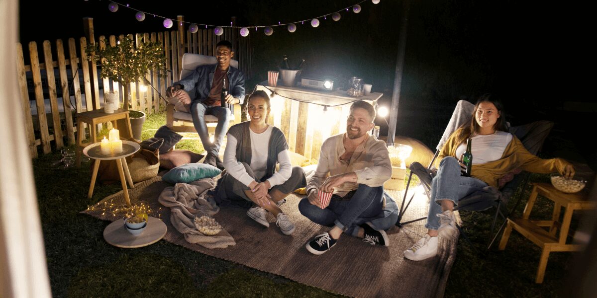 Friends enjoying an outdoor patio, seated around a stylish table with cozy seating, surrounded by warm lighting and a beautifully landscaped setting.